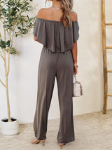 a woman wearing a grey jumpsuit and a white purse