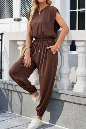 a woman leaning against a wall wearing a brown jumpsuit