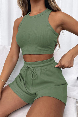 a woman sitting on a bed wearing a green top and shorts