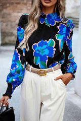 a woman wearing a black and blue floral blouse and white pants