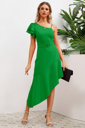 a woman in a green dress standing next to a plant