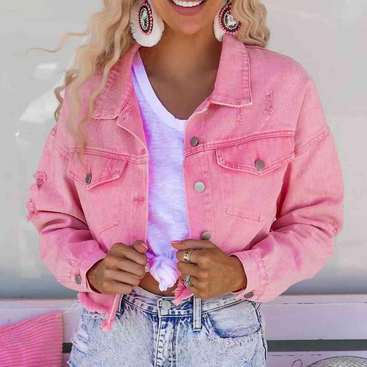 a woman wearing a pink jean jacket and earrings