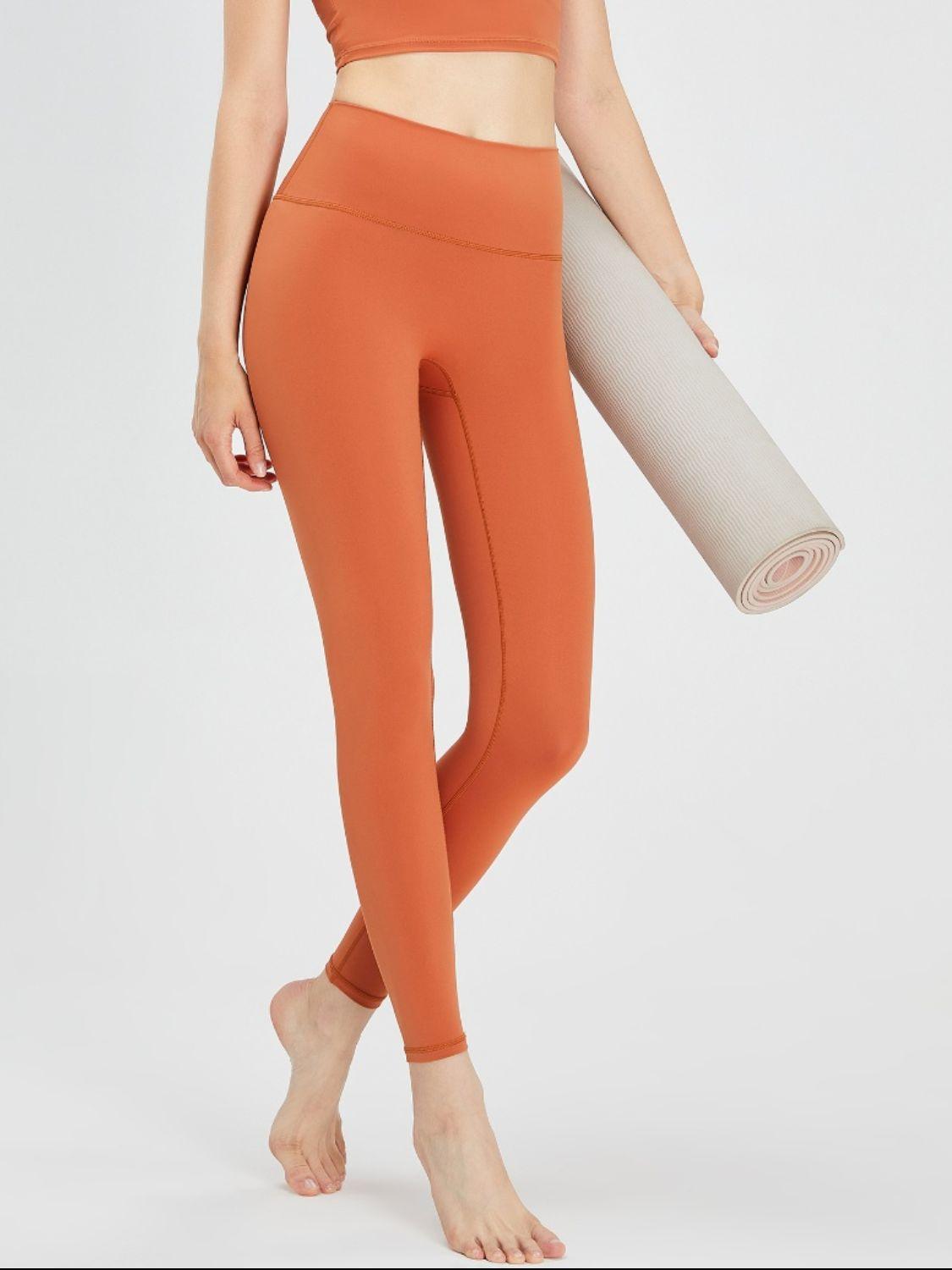a woman in an orange sports bra top and leggings holding a yoga mat