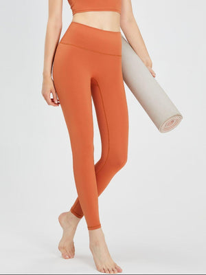 a woman in an orange sports bra top and leggings holding a yoga mat