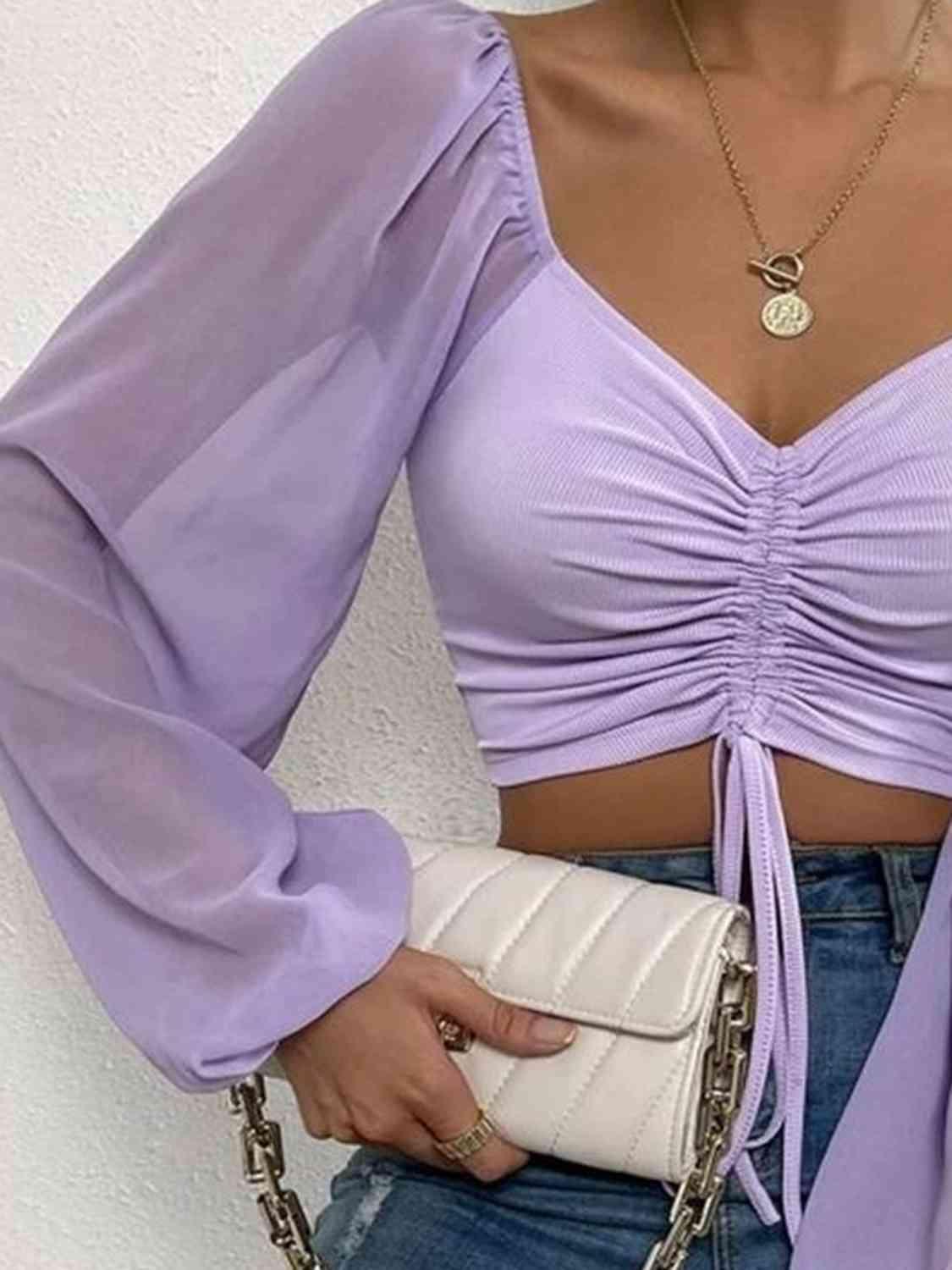 a woman wearing a purple top and jeans holding a white purse