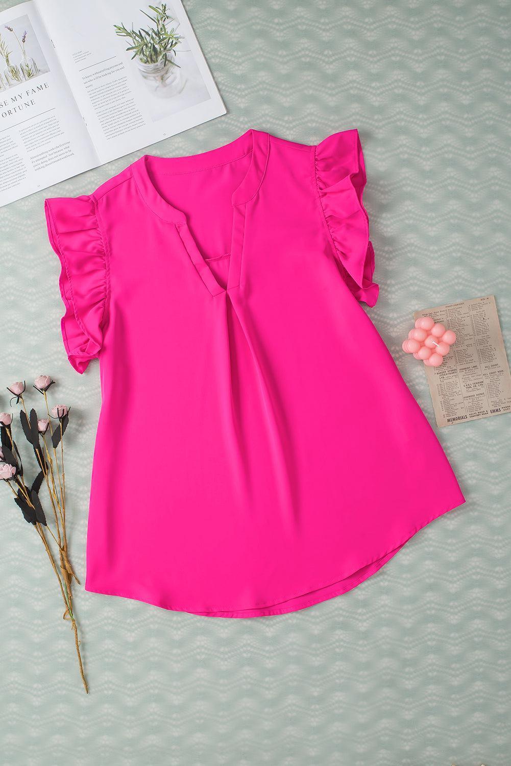 a pink blouse with ruffles and a flower on a table