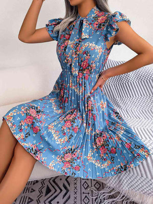 a woman sitting on a bed wearing a blue floral dress