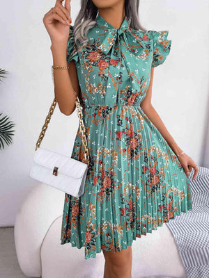 a woman in a green floral dress holding a white purse