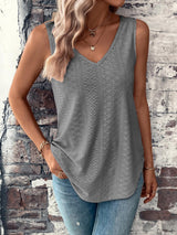 a woman standing against a brick wall wearing a gray tank top