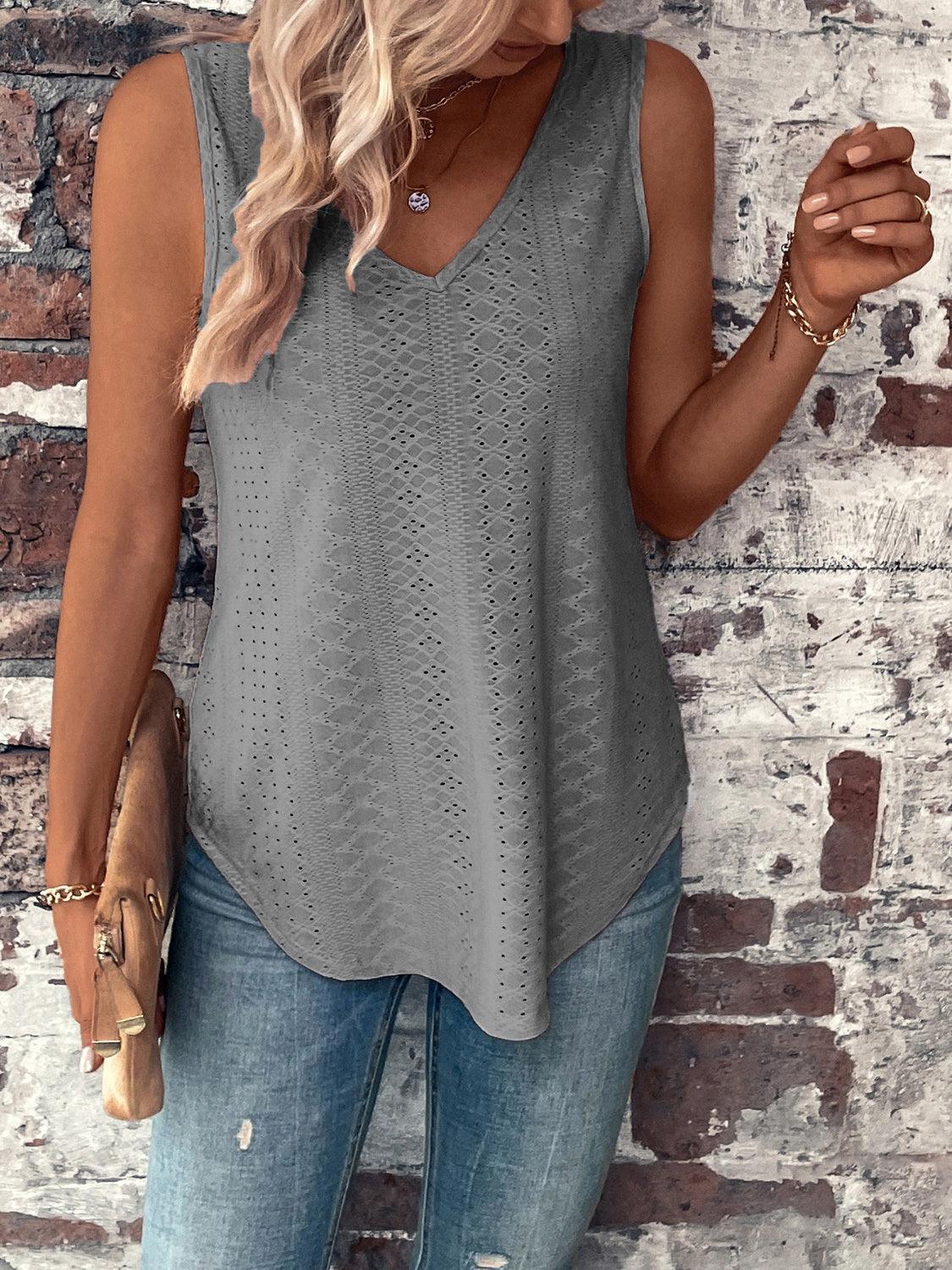 a woman standing against a brick wall wearing a gray tank top