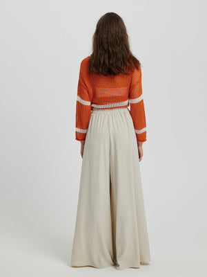 a woman in an orange sweater and cream wide legged pants