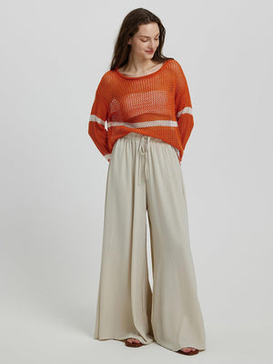 a woman in an orange sweater and wide pants