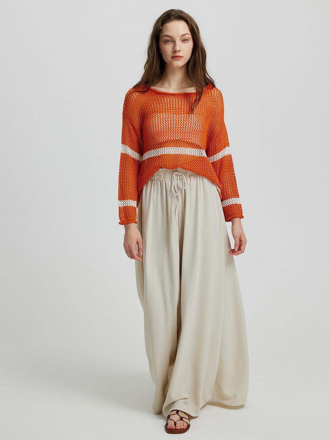 a woman in an orange sweater and beige pants