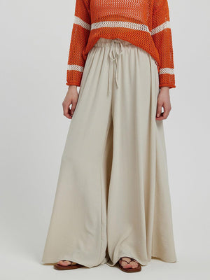 a woman in an orange sweater and beige wide legged pants