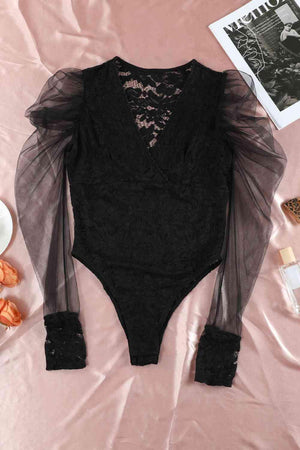 a black bodysuit with sheer sleeves on a pink sheet