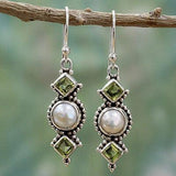 a pair of earrings with pearls and green stones