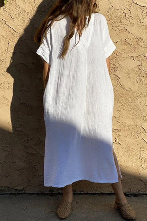 a woman standing against a wall wearing a white dress