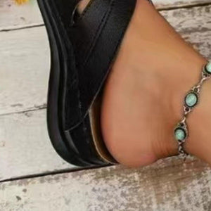 a woman's foot wearing a black sandals and a turquoise beaded bracelet