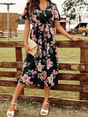 a woman in a floral dress leaning on a fence