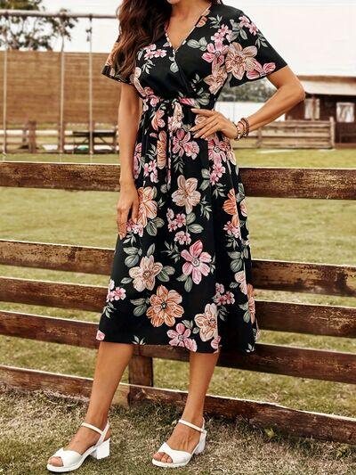 a woman wearing a black floral dress standing in front of a fence