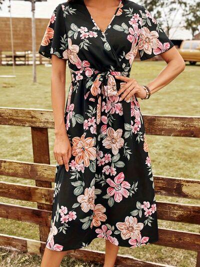 a woman standing in front of a fence wearing a black floral dress