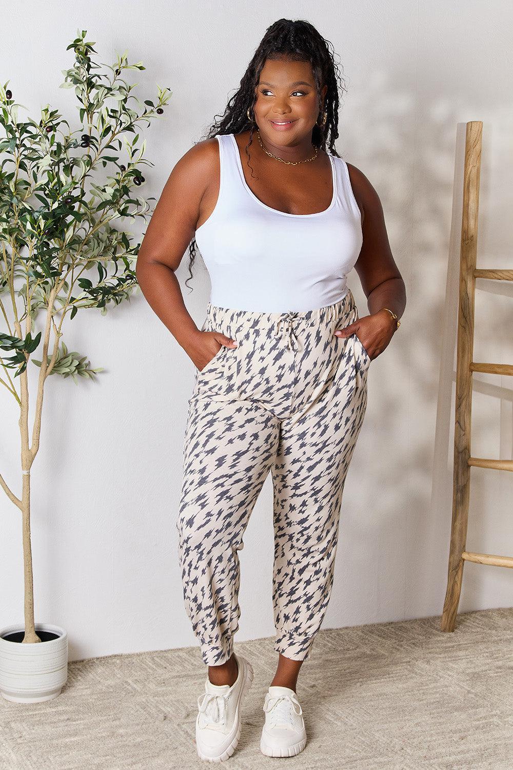 a woman in a white tank top and patterned pants