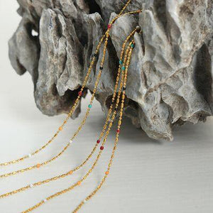 a gold necklace with multi - colored beads on a rock