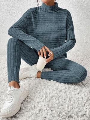 a woman sitting on the floor wearing a turtle neck sweater and pants