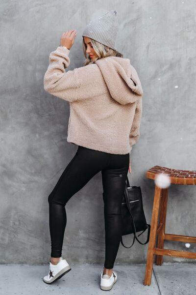 a woman leaning against a wall wearing a sweater and leggings