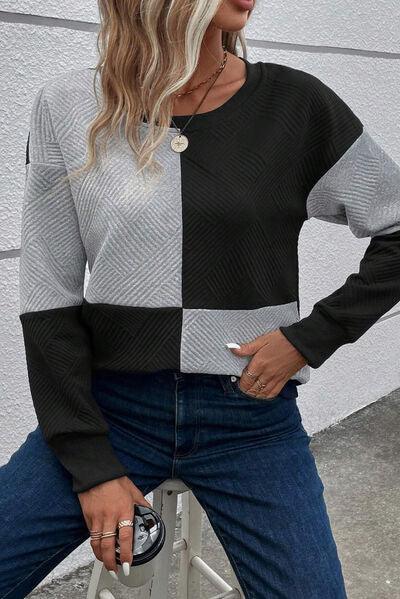 a woman sitting on a stool wearing a black and grey sweater