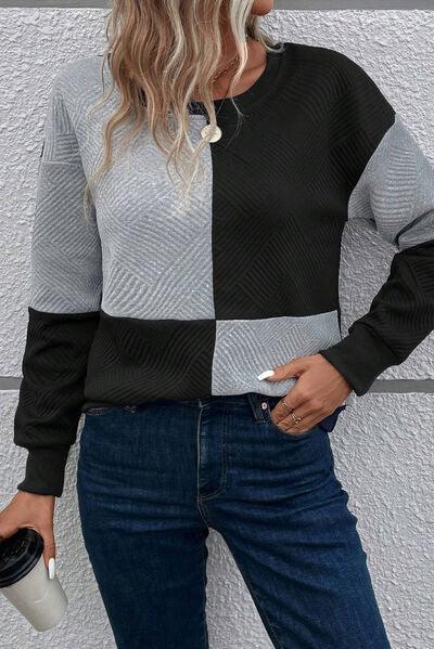 a woman standing against a wall wearing a black and grey sweater