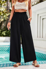 a woman standing in front of a pool wearing a crop top and wide legged pants