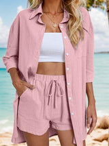 a woman standing on a beach wearing a pink shirt and shorts