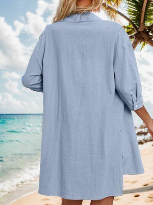 a woman standing on a beach wearing a blue shirt dress