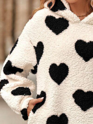 a woman wearing a white and black sweater with black hearts on it