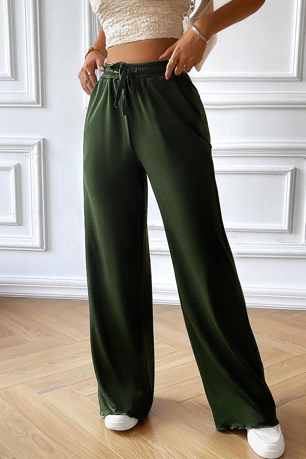 a woman standing on a wooden floor wearing green pants