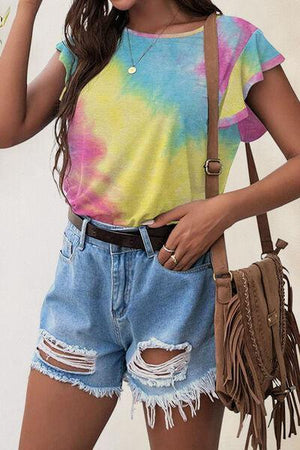 a woman wearing a tie dye shirt and denim shorts