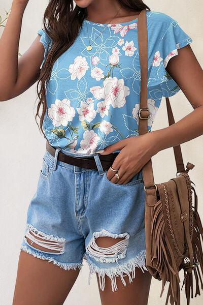 a woman wearing a blue floral shirt and denim shorts