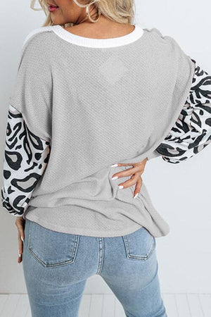 a woman wearing a grey sweater with black and white print sleeves