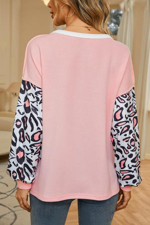 a woman wearing a pink top with leopard print sleeves