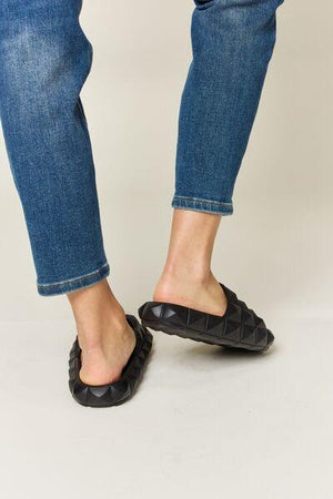 a woman's feet in a pair of blue jeans and black slippers