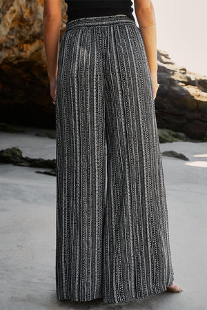 a woman standing on a beach wearing a black and white striped pants