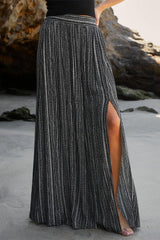 a woman standing on a beach wearing a black and white striped skirt