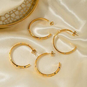 a pair of gold hoop earrings sitting on a white cloth