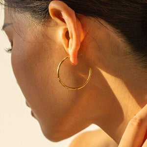 a woman wearing a pair of gold hoop earrings