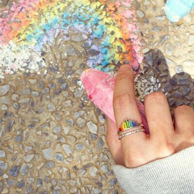 a person's hand holding a piece of paper with a rainbow painted on it