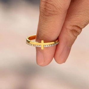 a woman's hand holding a gold ring with a cross on it