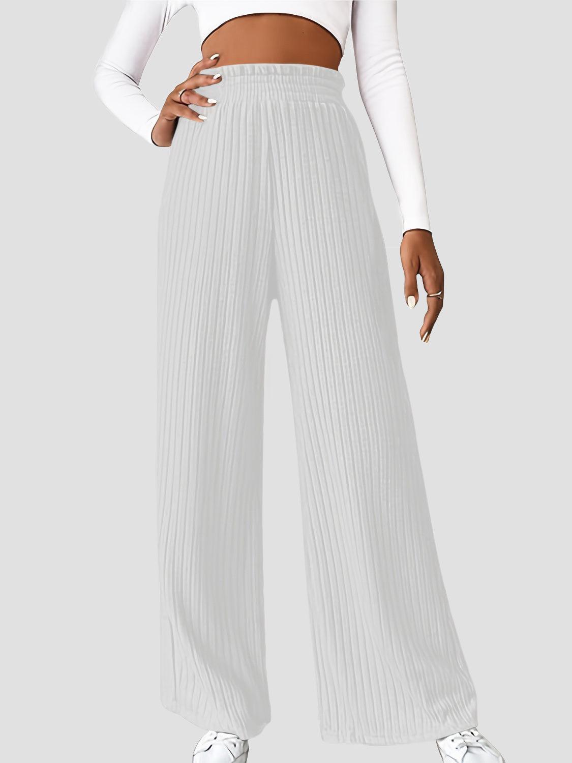 a woman wearing a white crop top and pleated pants